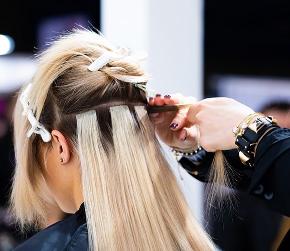 Professional hairdresser making hair extensions for blonde girl